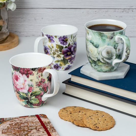 A set of three fine bone china mugs with floral chintz patterns, featuring designs Chintz White Roses, Rose Bouquet, and Purple Pansies sitting on a kitchen counter.